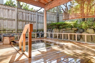 Una terraza de madera con un jacuzzi, rodeada por una valla de madera y un muro de piedra.