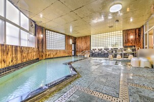 Una piscina interior con paneles de madera y paredes de azulejos, rodeada de zonas de estar y suelo de baldosas.
