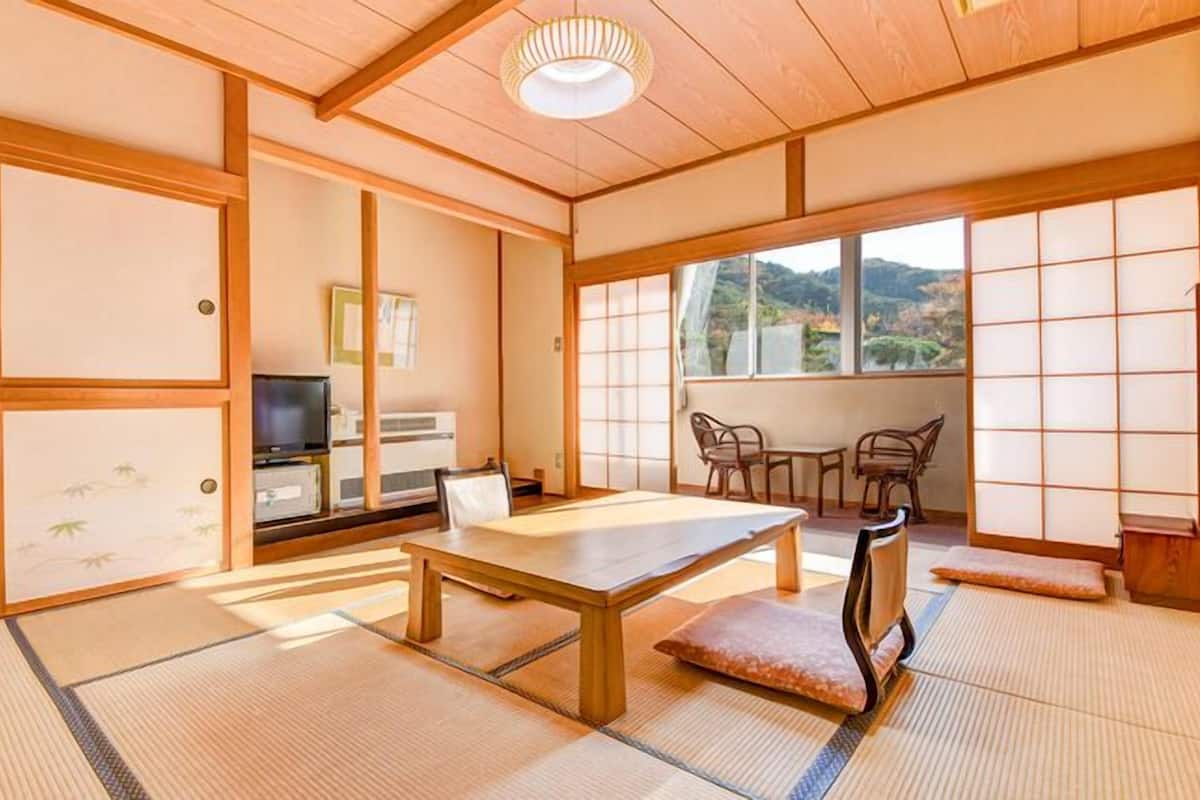 Perinteinen japanilainen huone, jossa on tatamimatto, matala pöytä, televisio ja suuret ikkunat, joista avautuu näkymä vuoristomaisemaan.