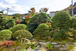 A traditional Japanese garden with a pond, rocks, and various trees.