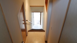 A narrow hallway with a wooden door on the left, a white door on the right, and a small window at the end.