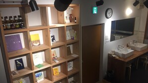 A room with wooden shelves displaying books and bottles, a clock, and a mirror.