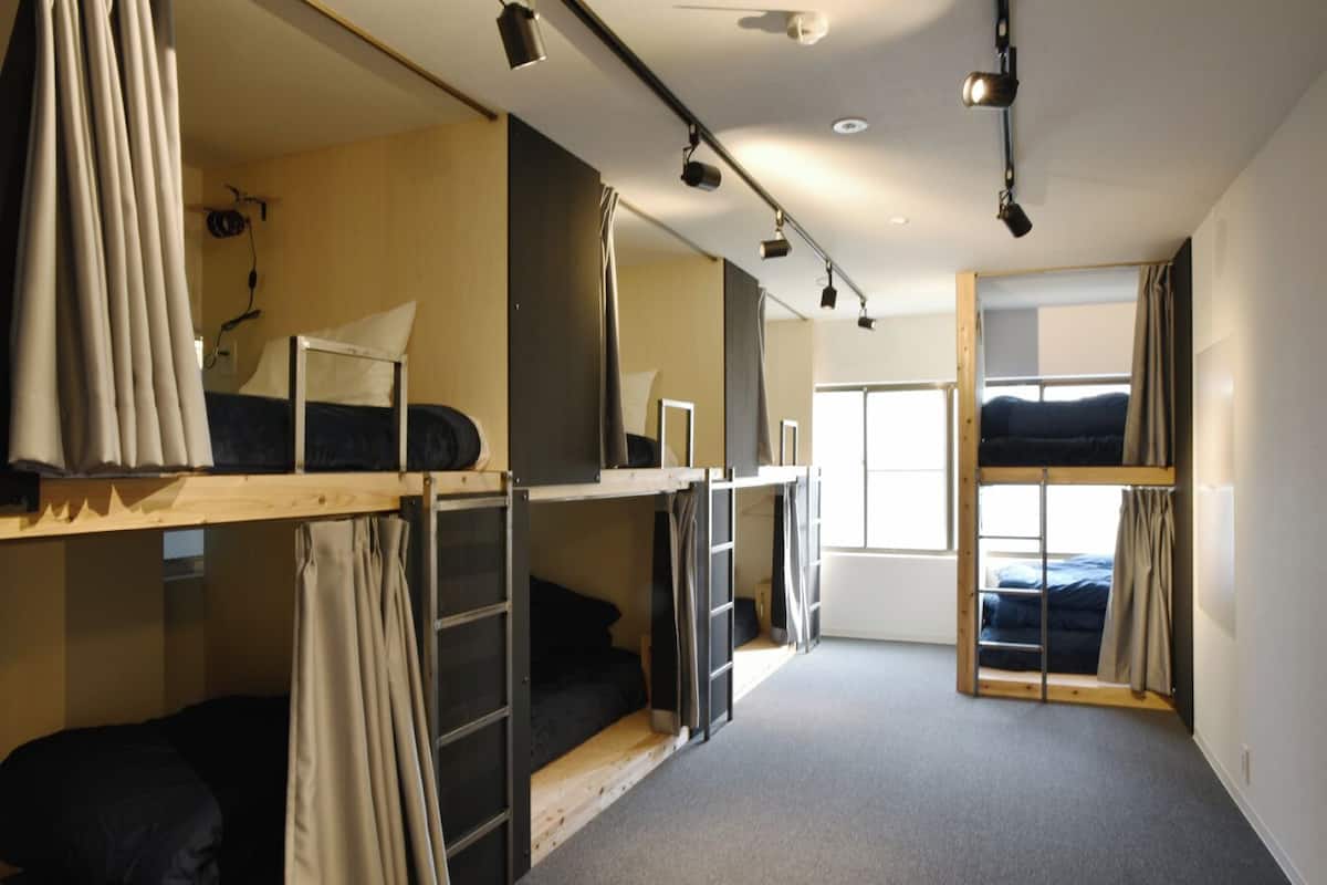 A dormitory room with bunk beds, a window, and a ceiling light fixture.