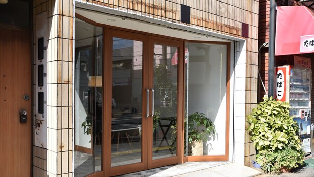 A hostel with a wooden exterior, large glass doors, and a small potted plant outside.
