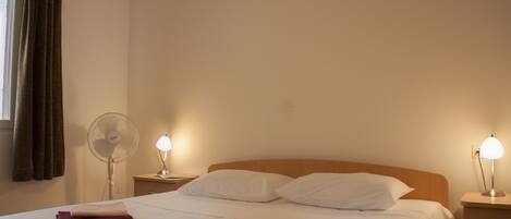 A neatly made bed with white and brown towels, a bedside fan, and a lamp on a wooden nightstand.