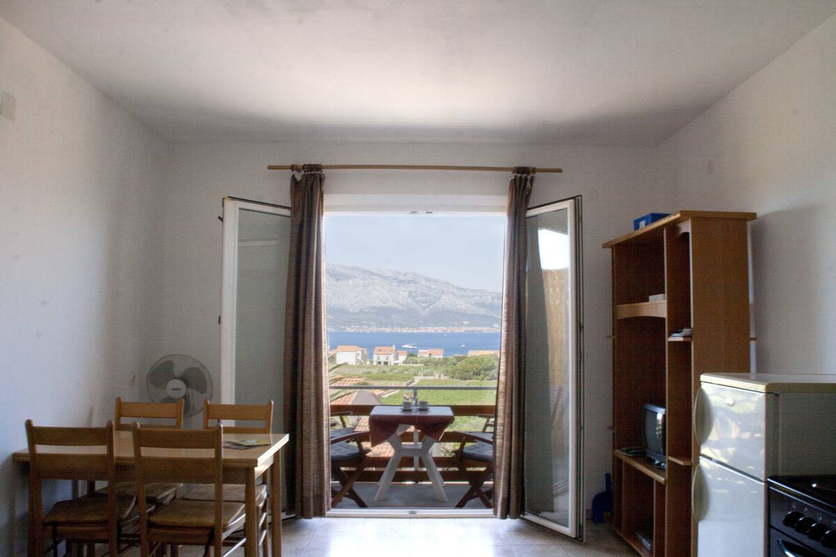 Et værelse med balkon, spisebord med stole, ventilator og køleskab.