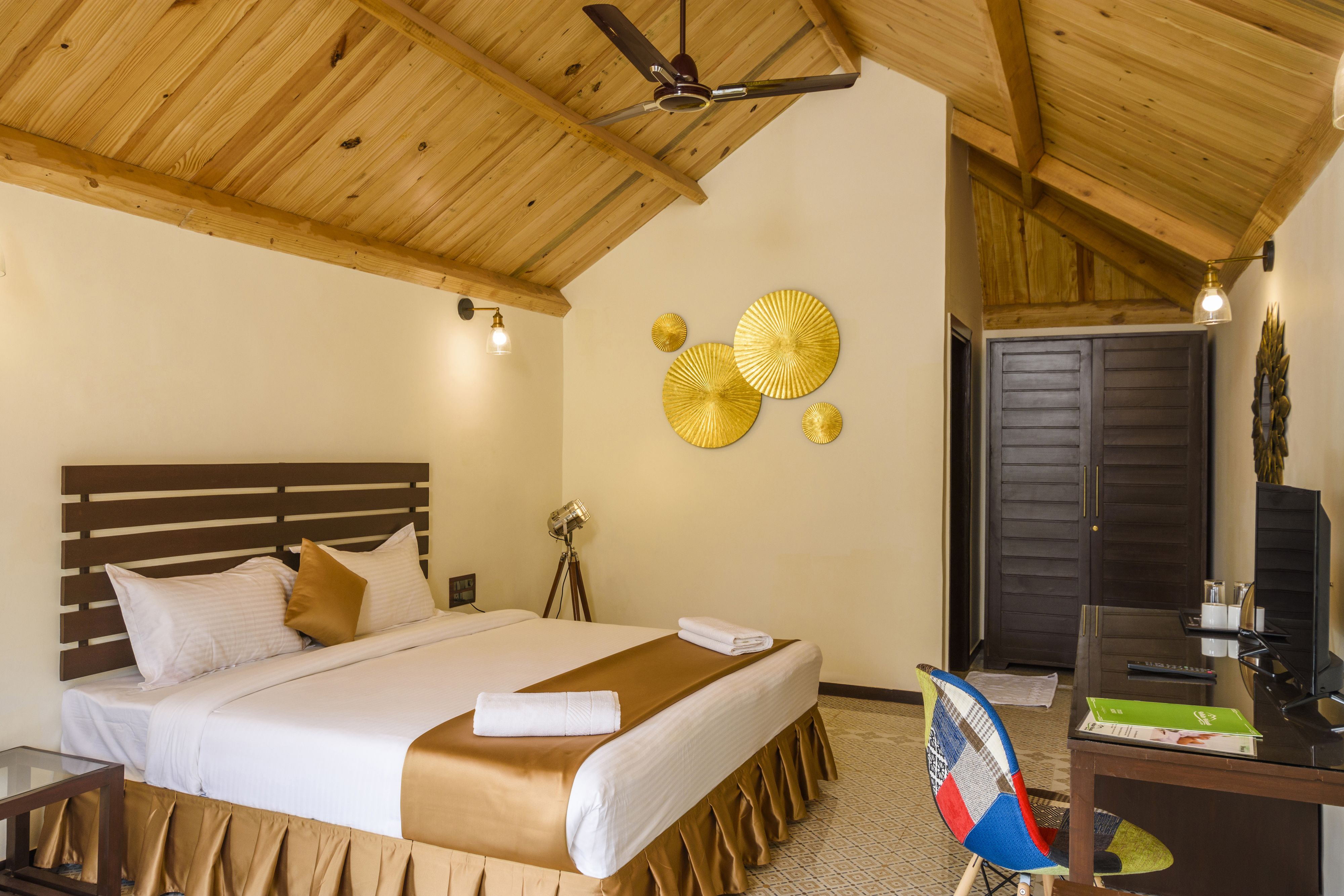 A hotel room with a wooden ceiling, a bed with white linens, a desk with a chair, and decorative wall art.