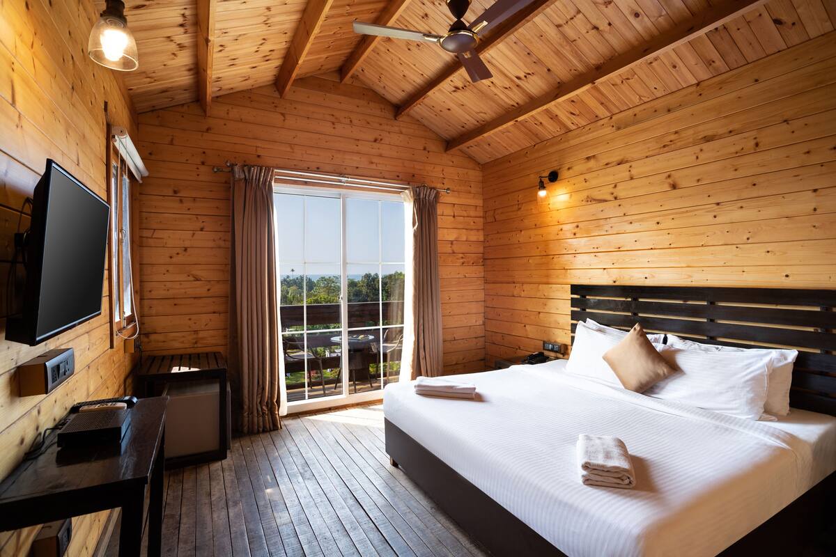 A wooden cabin room with a bed, a TV, and a desk.