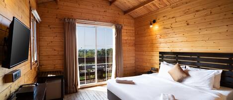 A wooden cabin room with a bed, a TV, and a desk.