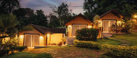A bungalow-style hotel with a well-maintained lawn, a patio with outdoor furniture, and a staircase leading to the entrance.