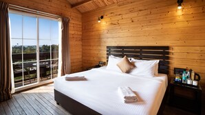 A wooden-paneled room with a large bed, a nightstand, and a view through a window. - Stone Wood Resort (Mandrem)