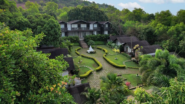 A multi-story building with a garden courtyard, surrounded by lush greenery and hills in the background. - Stone Wood Resort (Mandrem)