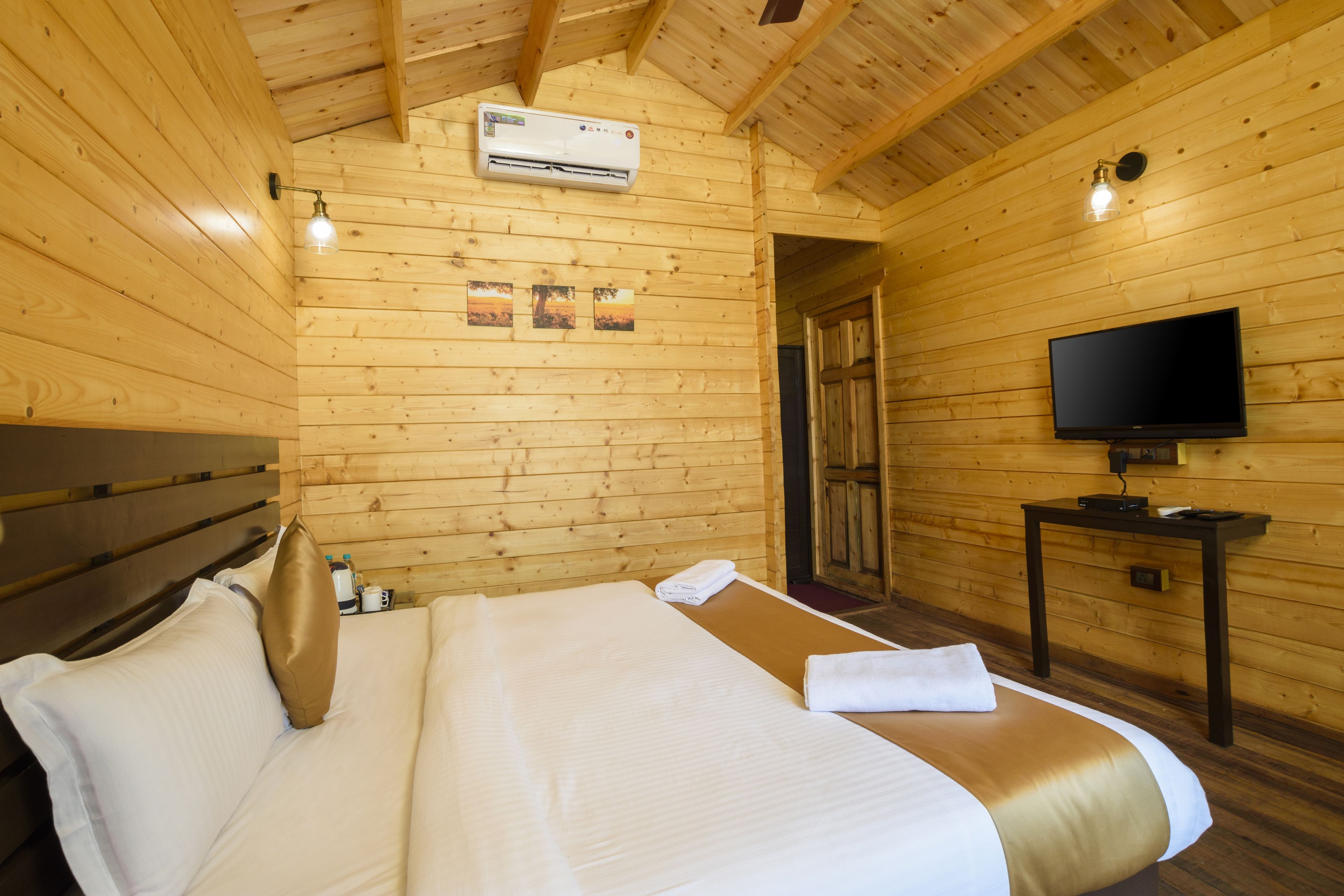 A wooden-paneled room with a bed, a flat-screen TV, and an air conditioning unit.