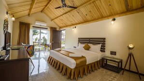 A hotel room with a wooden ceiling, a bed with a headboard, a desk with a chair, a small table, and a lamp. - Stone Wood Resort (Mandrem)