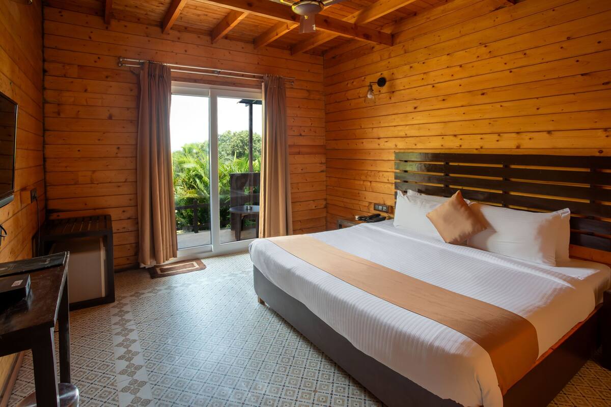 A wooden room with a bed, a desk, and a sliding glass door leading to an outdoor area.