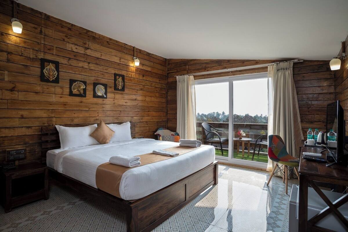 A wooden-paneled room with a large bed, a desk with a chair, and a view of the outdoors.