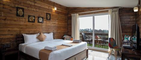 A wooden-paneled room with a large bed, a desk with a chair, and a view of the outdoors.