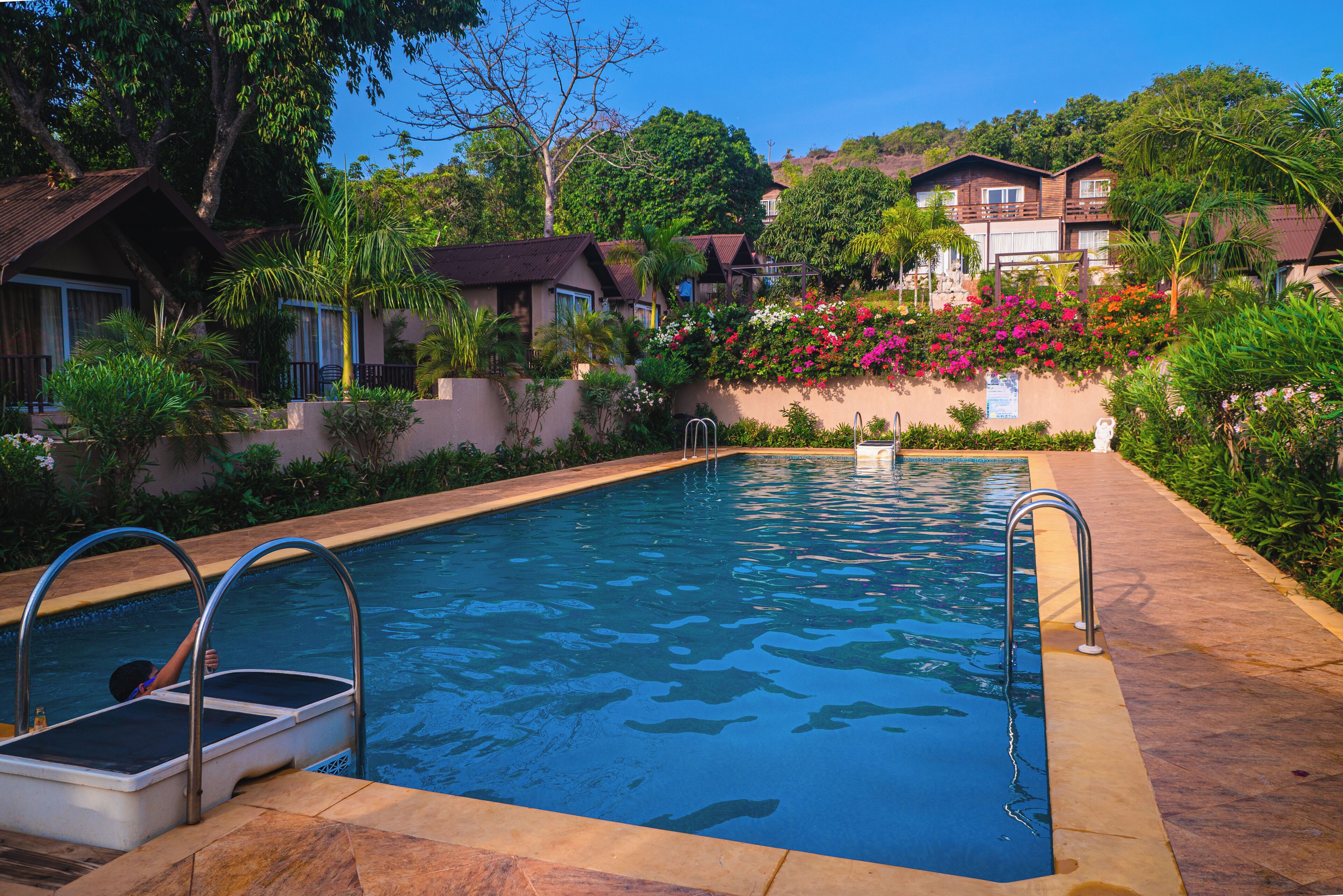 A rectangular swimming pool with metal ladders on both sides, surrounded by a stone deck.