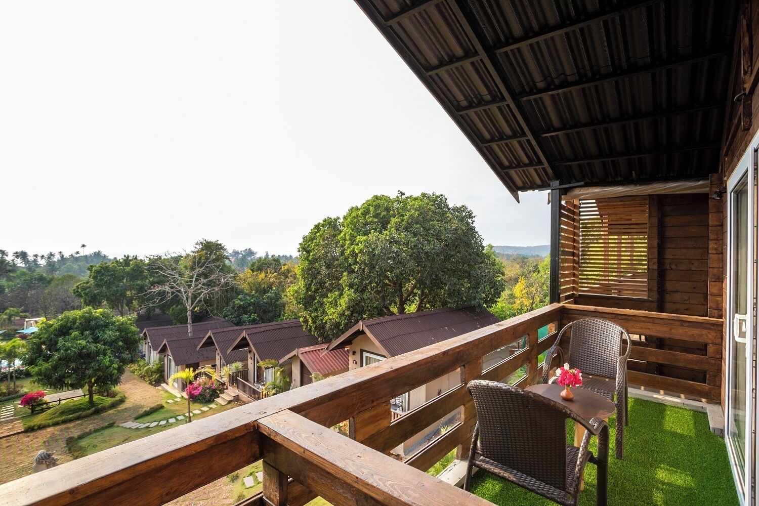 Ein Balkon mit Holzgeländer, der auf einen Garten mit mehreren Häusern und Bäumen blickt.