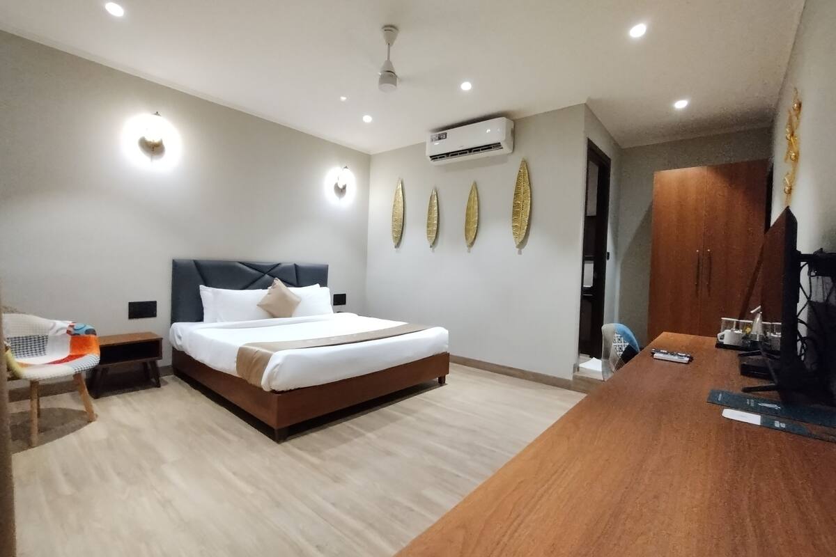 A modern hotel room with a bed, bedside table, chair, desk, and decorative wall art.