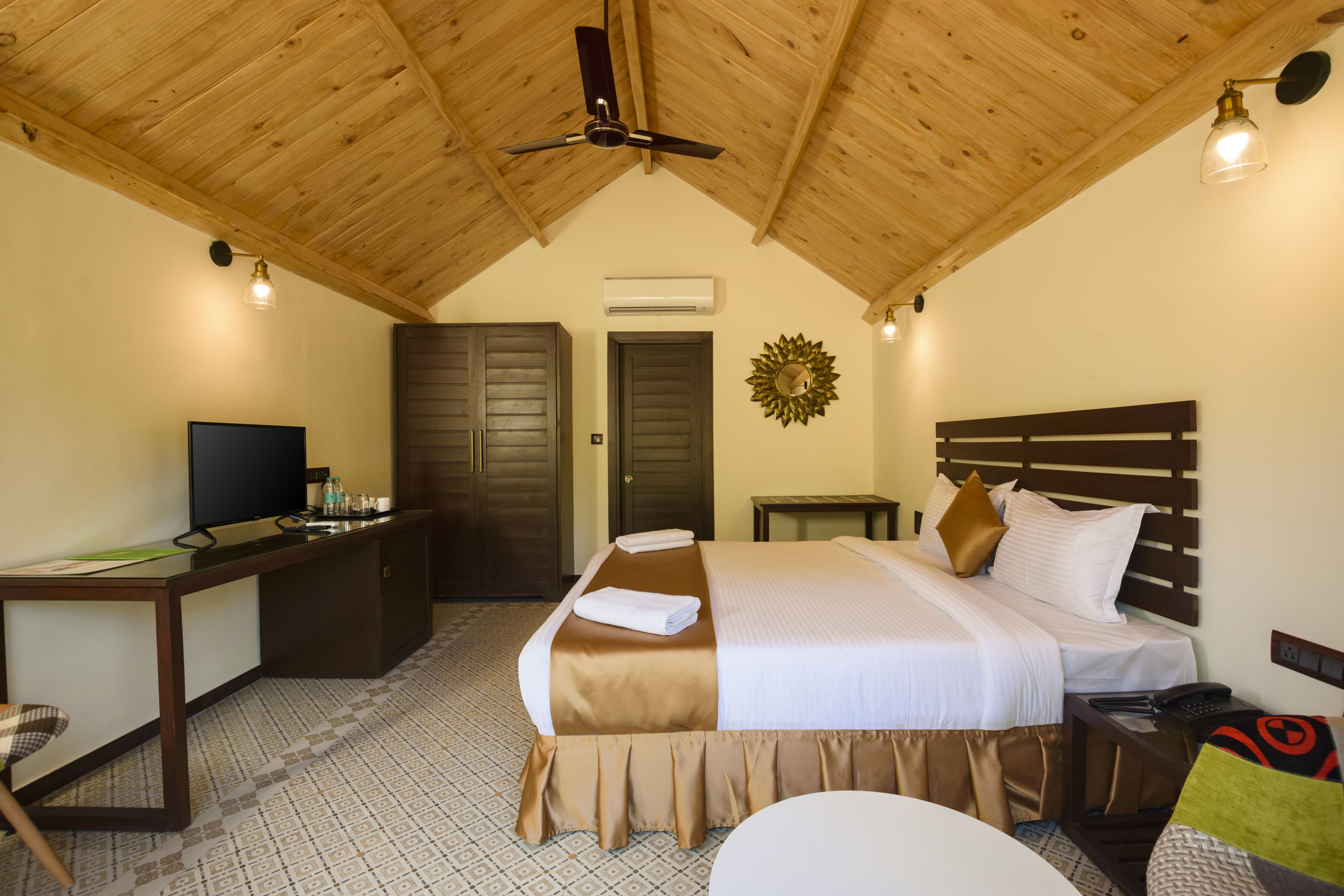 Une chambre d’hôtel avec un plafond en bois, un lit avec une tête de lit, un bureau avec une télévision et un climatiseur fixé au mur.