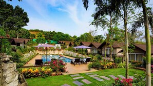 A resort with multiple bungalow-style buildings, a swimming pool, and a well-maintained garden with stepping stones. - Stone Wood Resort (Mandrem)