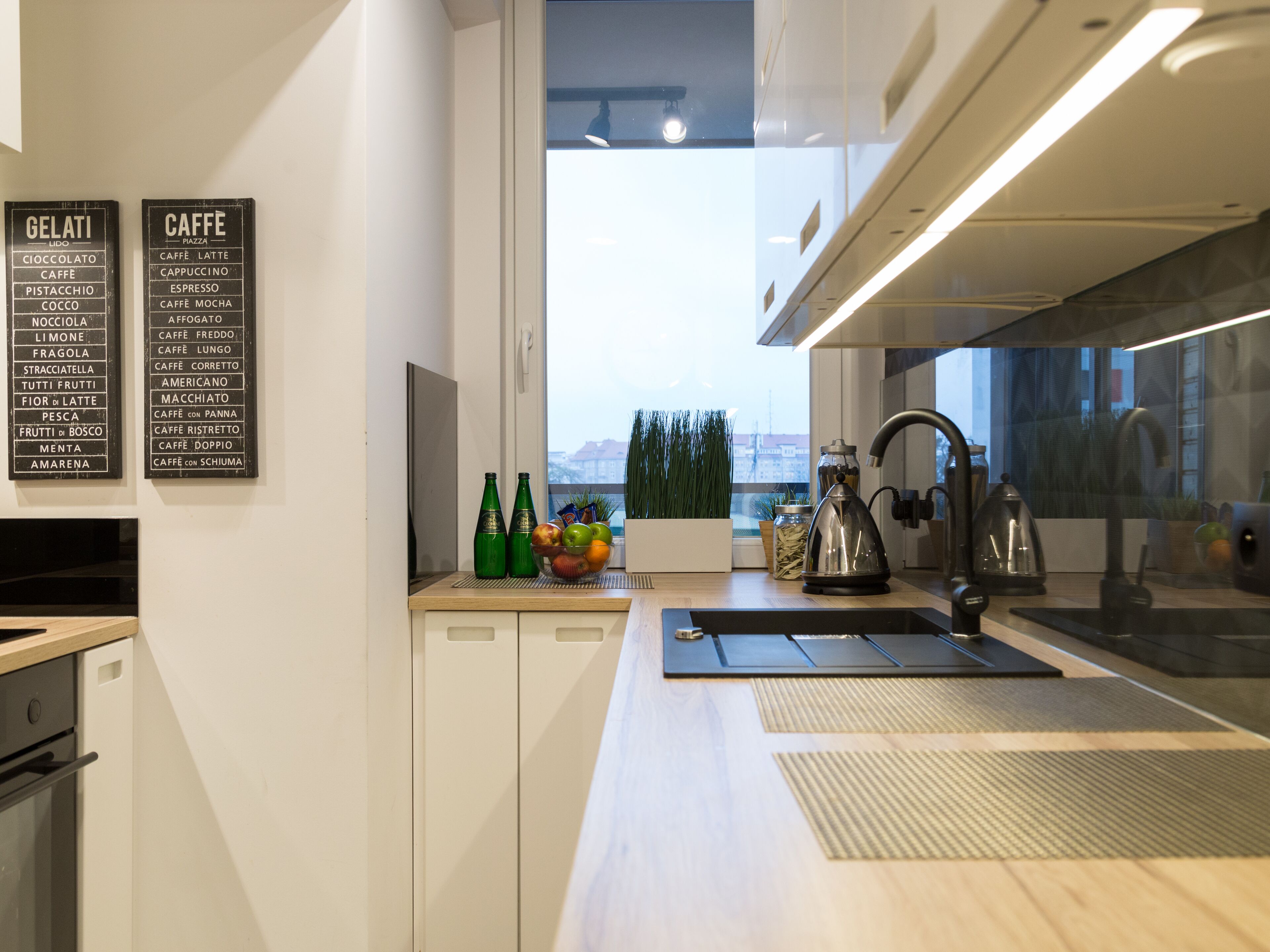 Una cucina moderna con vista sulla città. Si vedono un menu delle caffetterie, una ciotola di frutta e un bollitore.