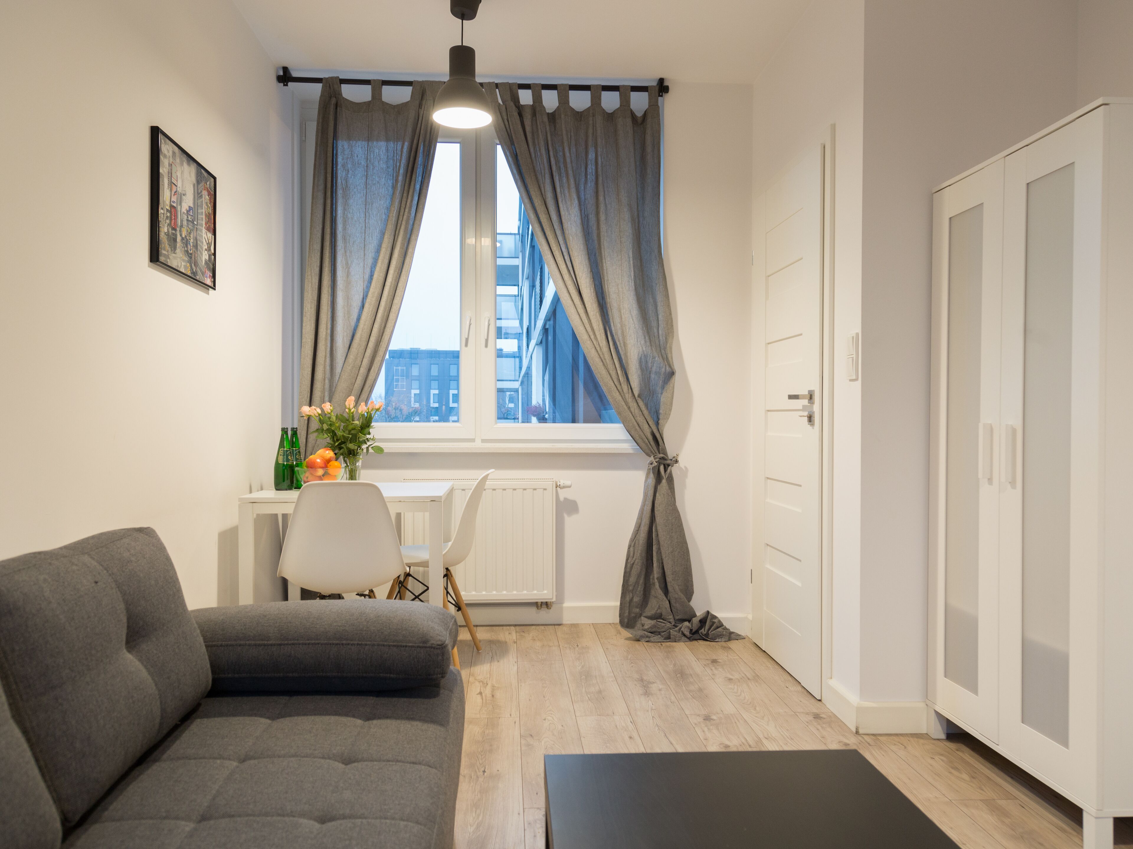Un salón moderno con un sofá gris, una mesita con un florero y una ventana con cortinas.