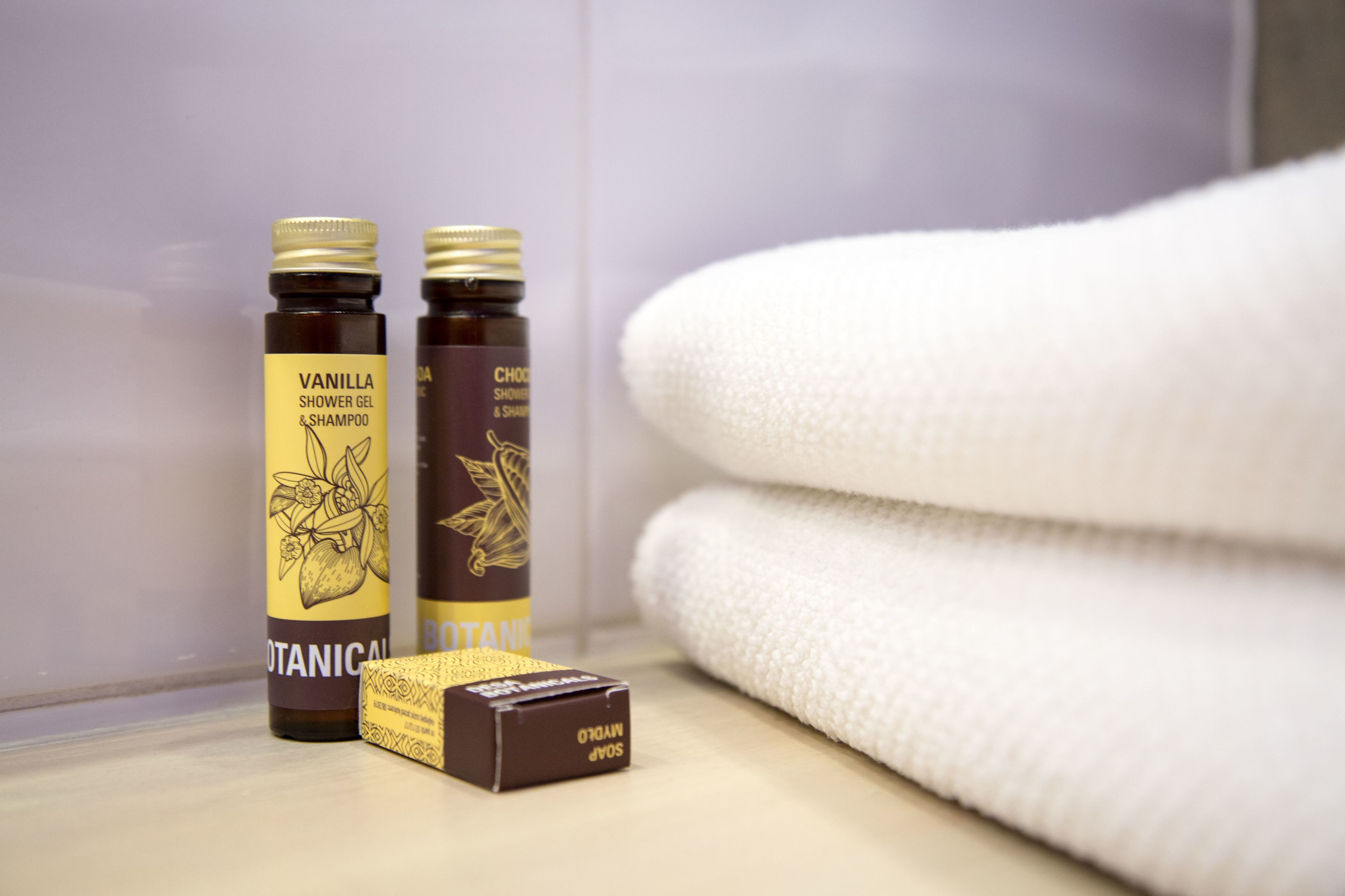 Deux bouteilles de gel douche et de shampoing, un savon et une serviette blanche pliée, posés sur le comptoir de la salle de bain.