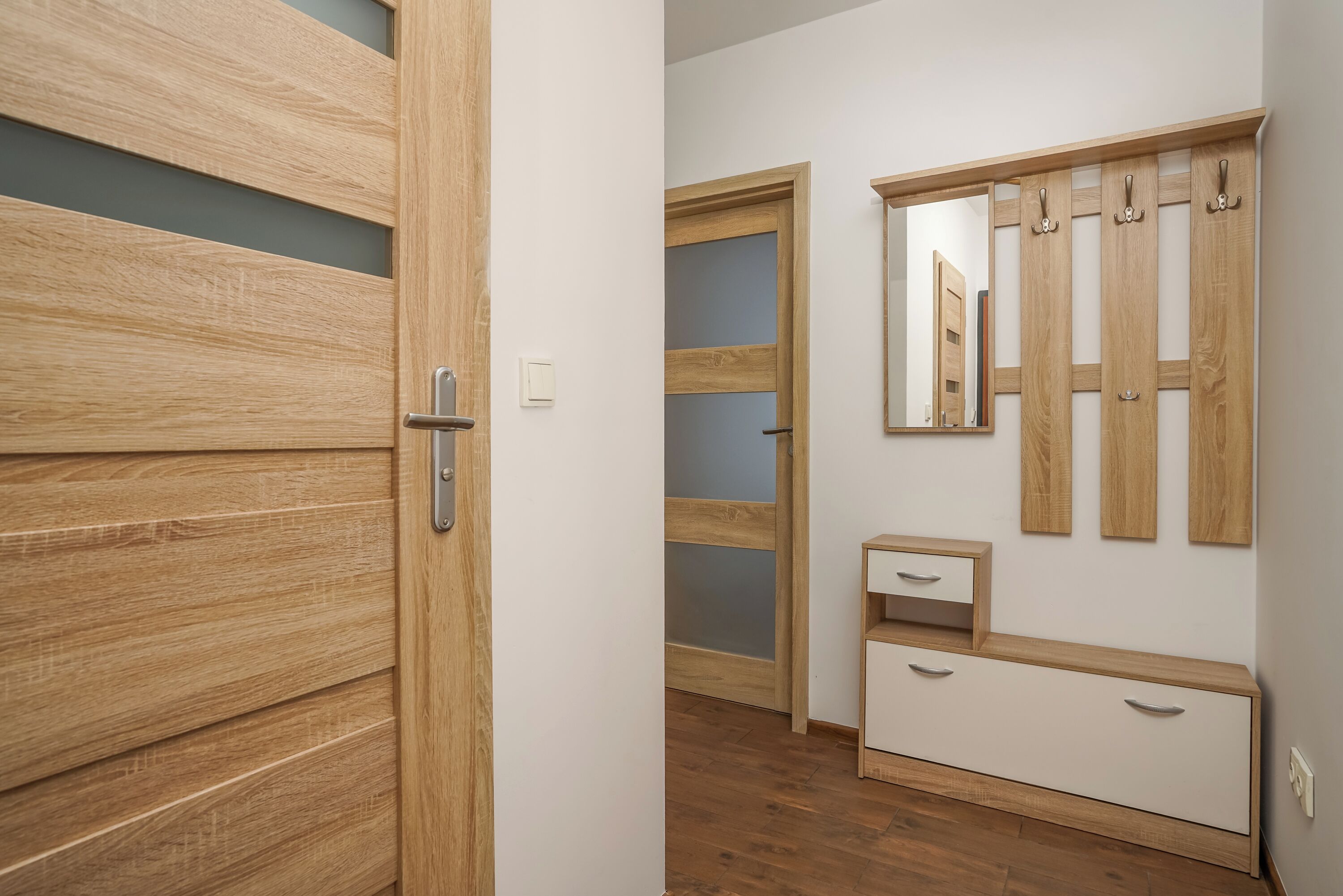 Une chambre moderne avec une armoire en bois, un miroir et un petit meuble de rangement.