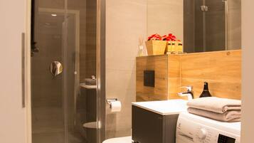 A modern bathroom with a glass-enclosed shower, a toilet, a sink, and a washing machine.
