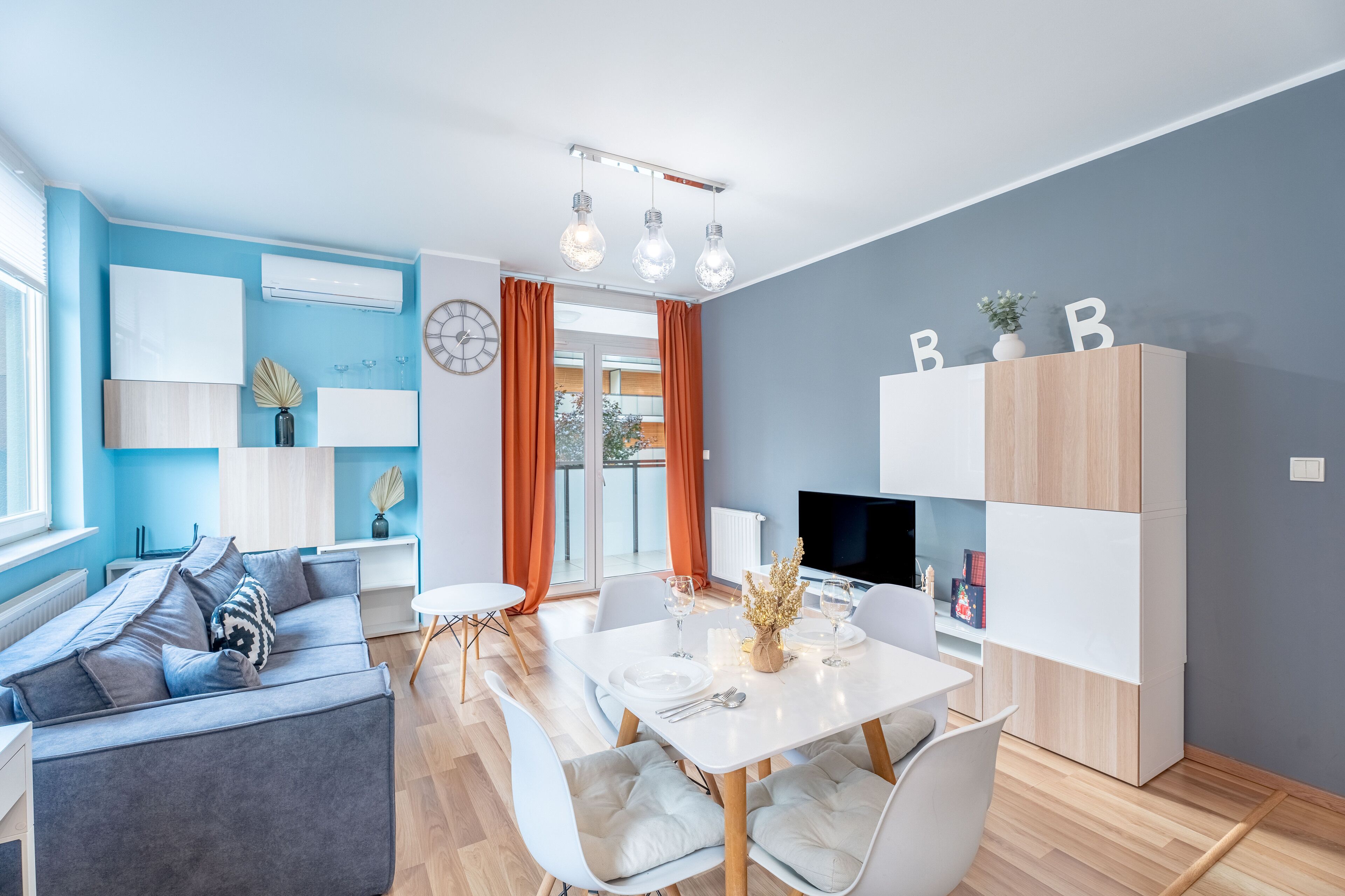 A modern living room with a sofa, dining table, and chairs, a TV, and a bookshelf.