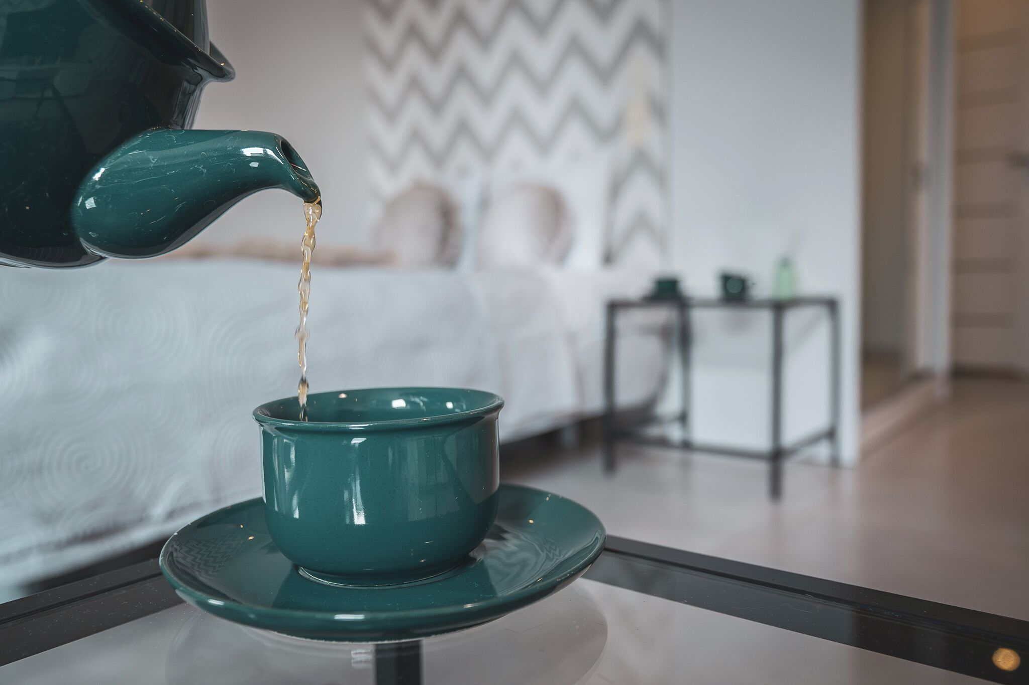 A green teapot pouring tea into a matching teacup on a table.