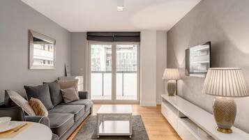 A modern living room with a grey sofa, a white coffee table, and a TV on a white stand.