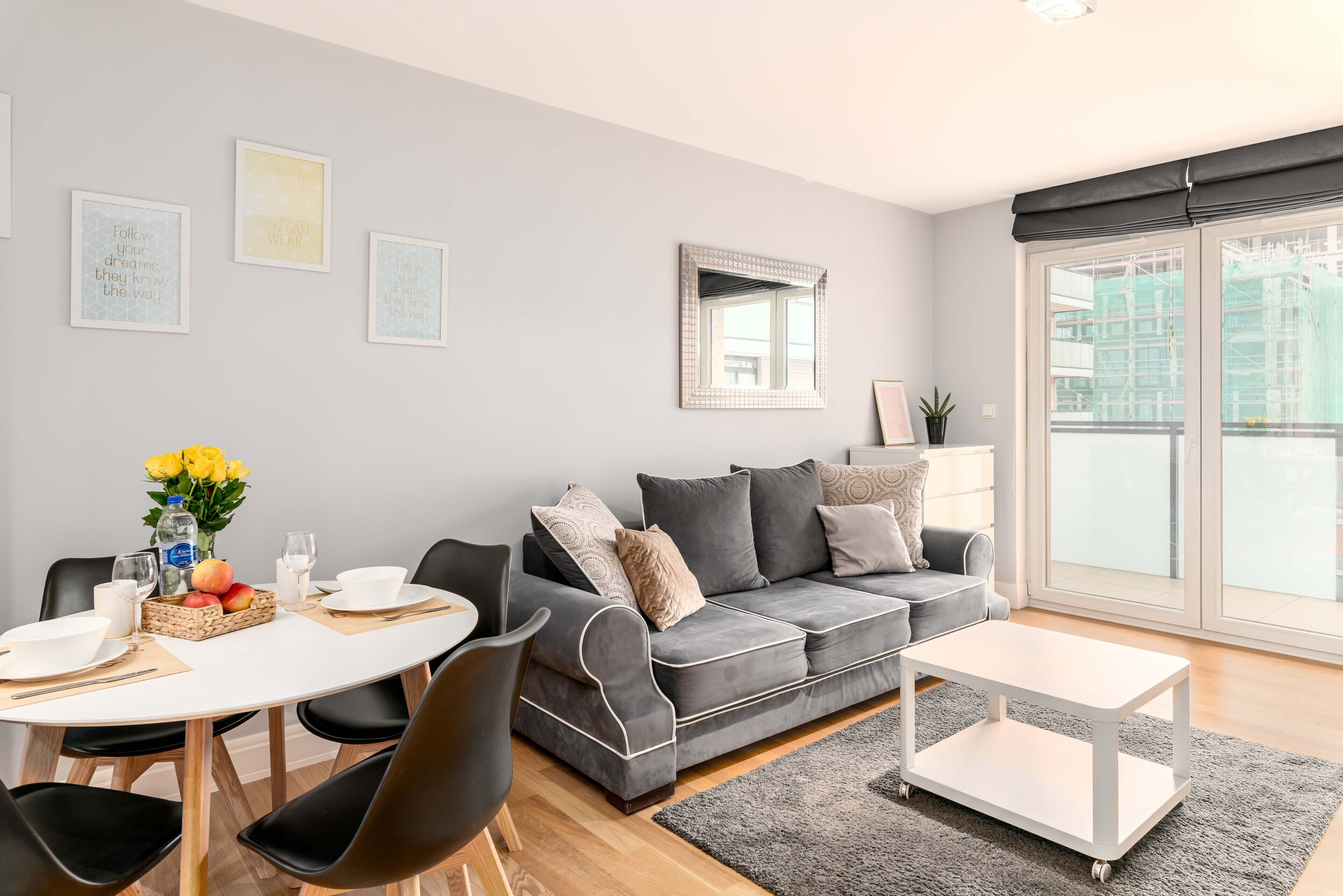 A modern living room with a grey sofa, a white coffee table, and a dining area with a round table and chairs.