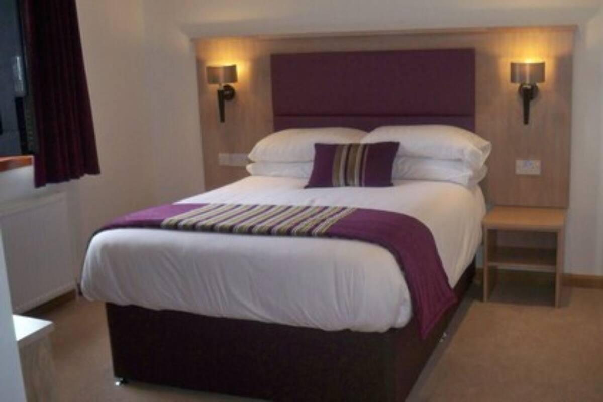 A bedroom with a bed, bedside lamps, a nightstand, and a window with curtains.
