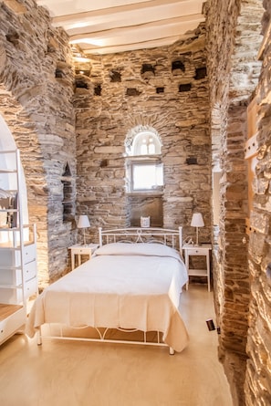 A bedroom with stone walls, a bed, bedside tables, and a window with a decorative arch.