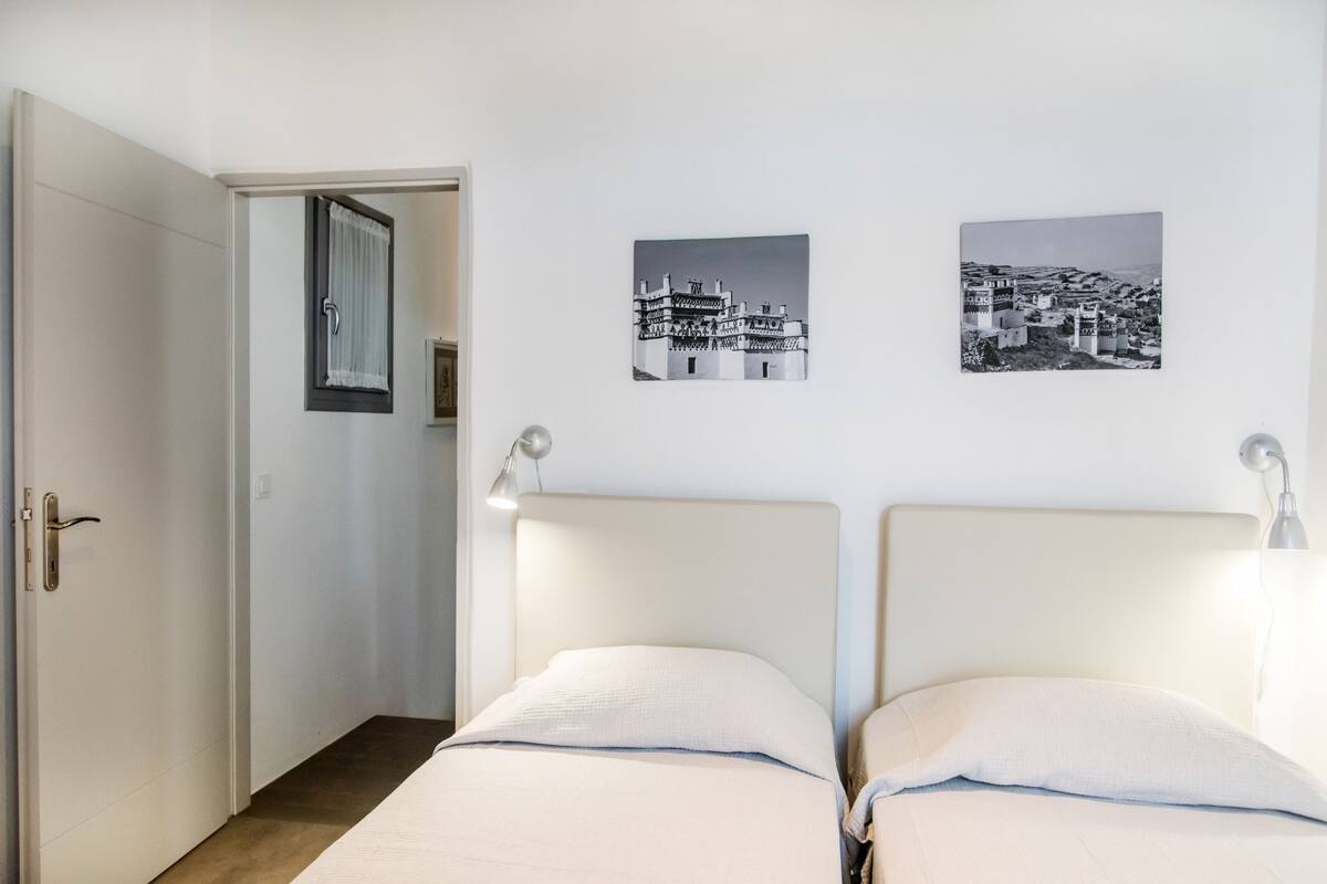 Une chambre avec deux lits, une porte et deux photographies en noir et blanc accrochées au mur.