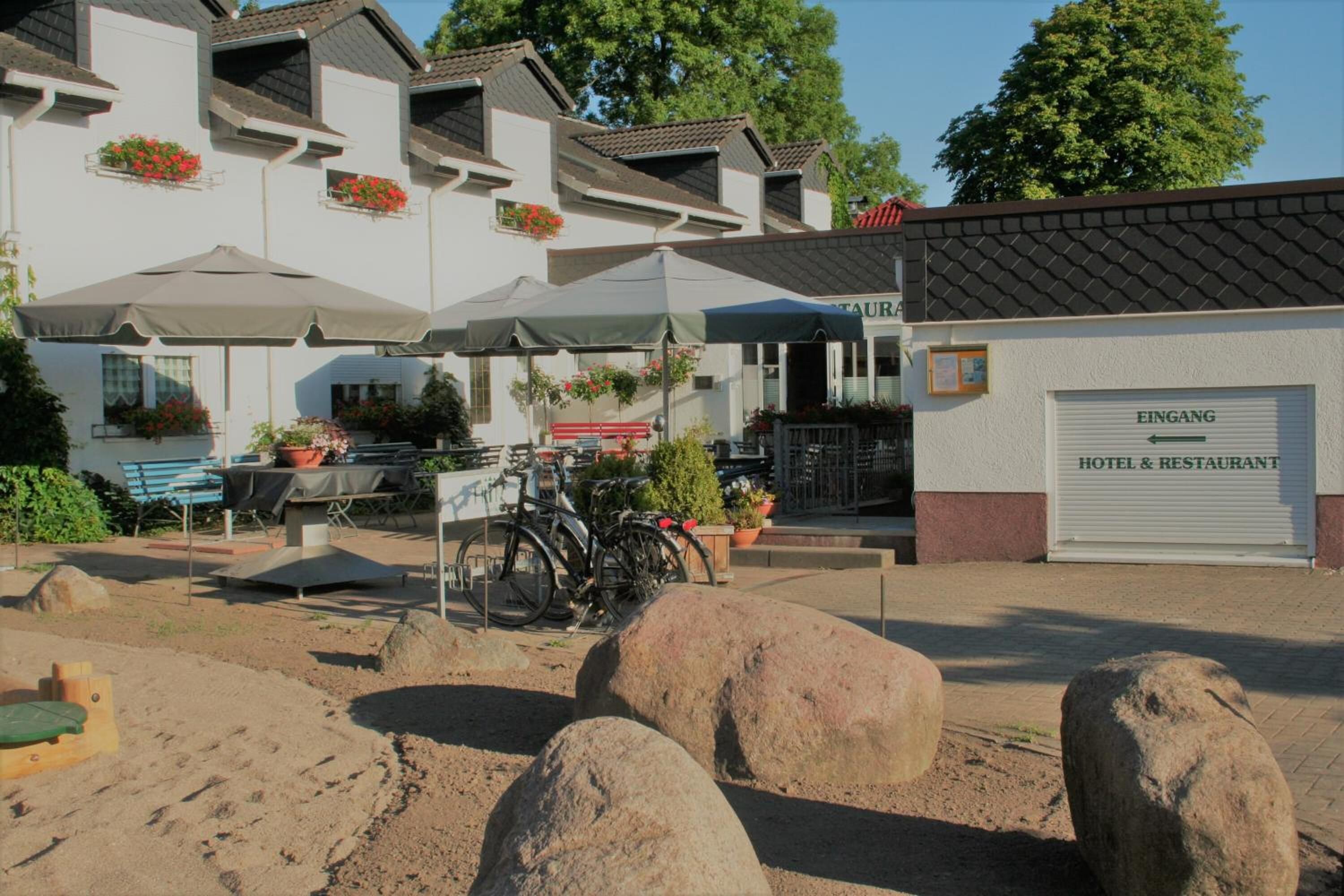 Hotel med udendørs siddepladser, cykler og en garage med skiltet "EINGANG HOTEL & RESTAURANT".