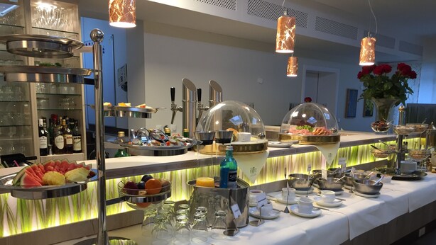 A buffet setup with various food items, a wine selection, and a decorative vase with red flowers. - Das Fritz Hotel (Schwerin)