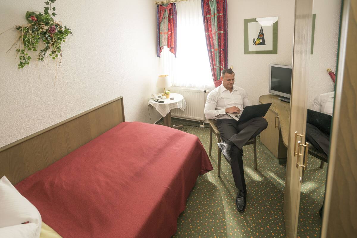 A hotel room with a single bed, a desk with a computer, a chair, and a television.