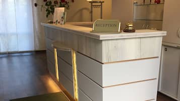 Una mesa de recepción con un cartel que dice 'RECEPTION', suelo de madera y una alfombra verde con el texto 'FRITZ HOTEL'.