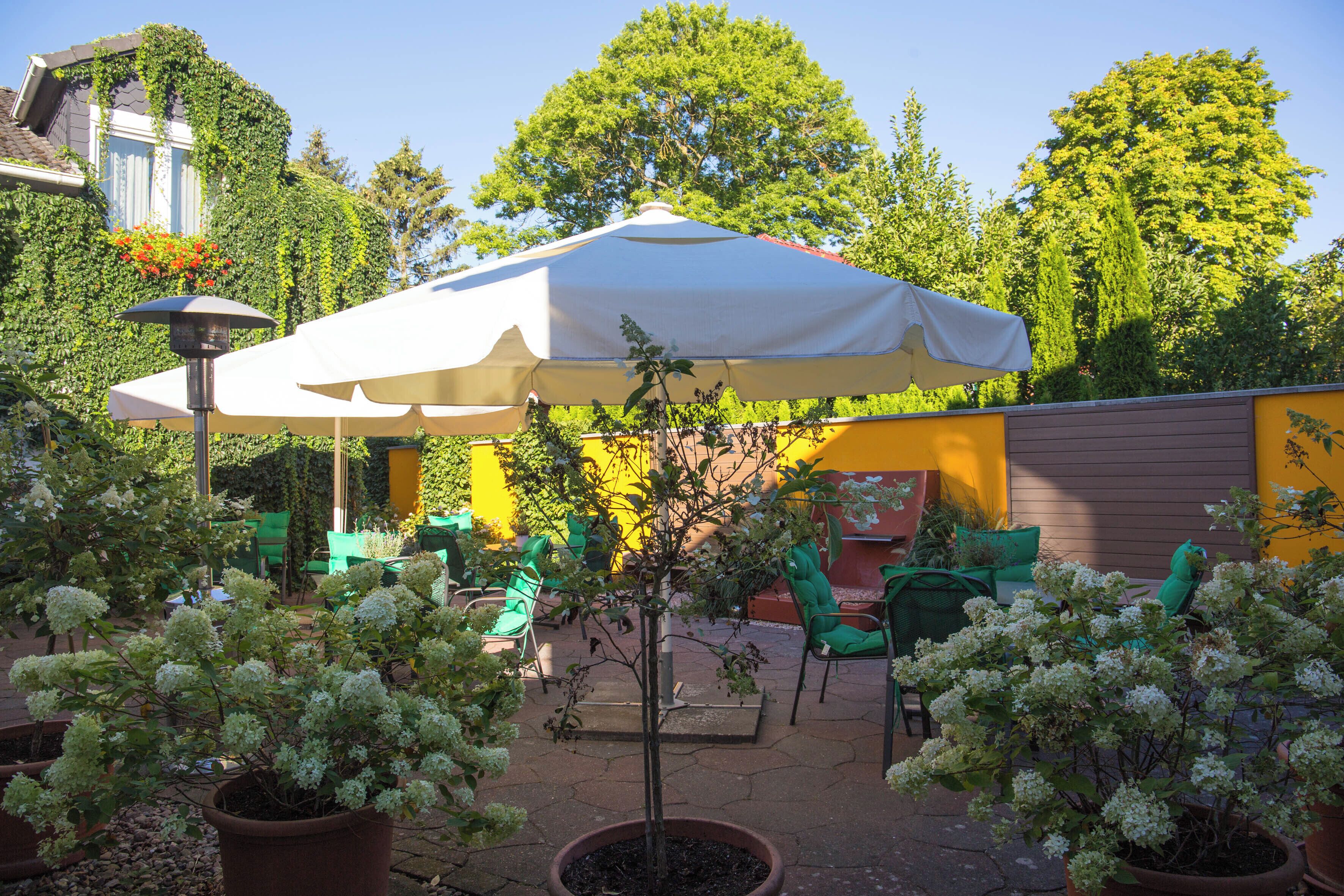 An outdoor patio area with a white umbrella, green chairs, and potted plants.