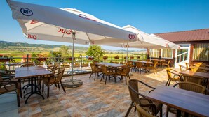 An outdoor patio with tables and chairs, large umbrellas, and a view of the countryside. - Hotel Europa Kokeltal (Albesti)