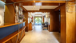 A reception area with a wooden reception desk, a blue counter, a leather sofa, and a glass door leading to an outdoor area. - Hotel Europa Kokeltal (Albesti)