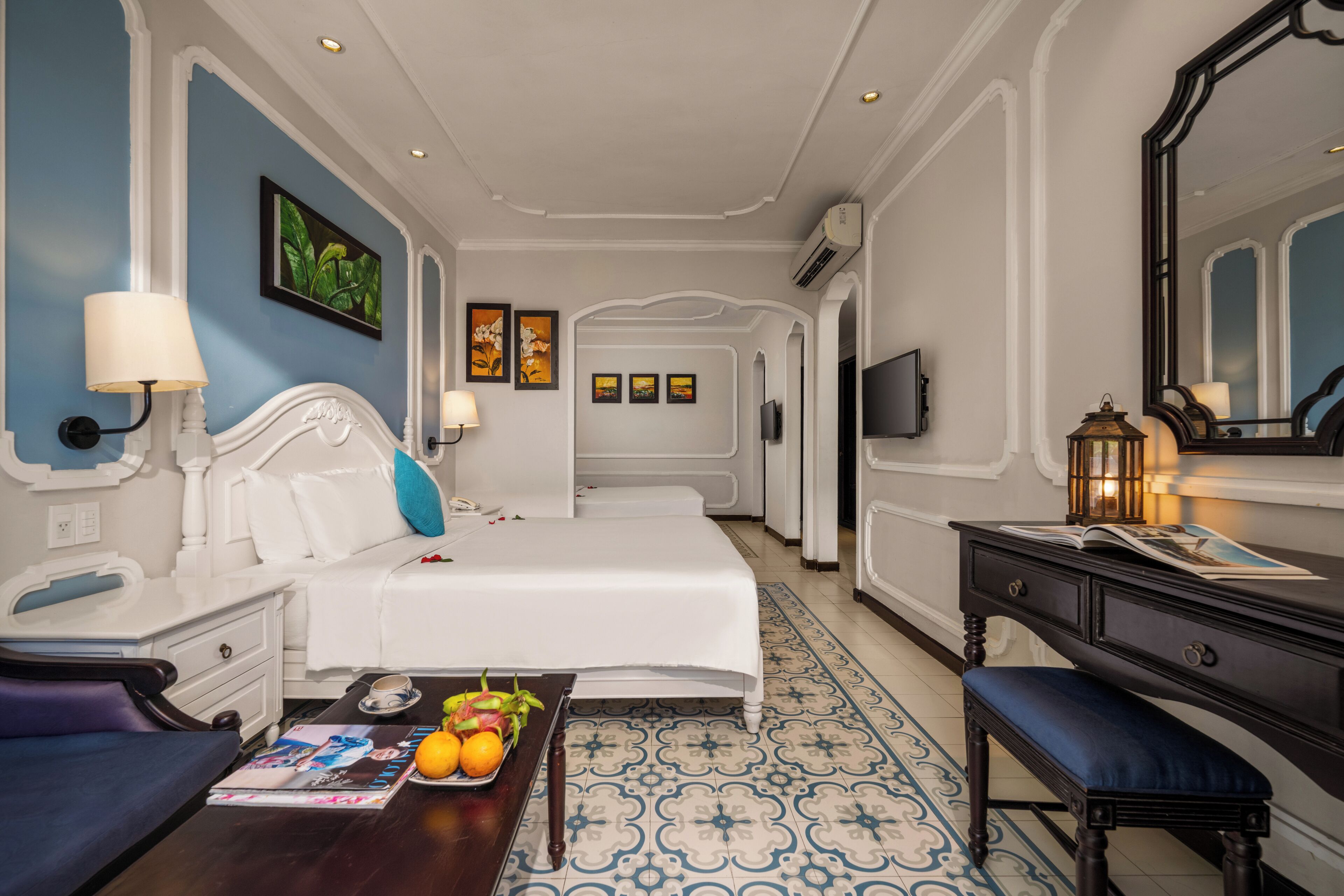 Une chambre d’hôtel comprenant un lit, des tables de chevet, un bureau, une chaise, une télévision et un miroir décoratif.