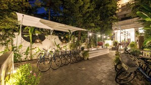 A paved outdoor area with bicycles parked under a canopy, surrounded by lush greenery and potted plants. - Hoi An Rosemary Boutique Hotel & Spa (Da Nang)