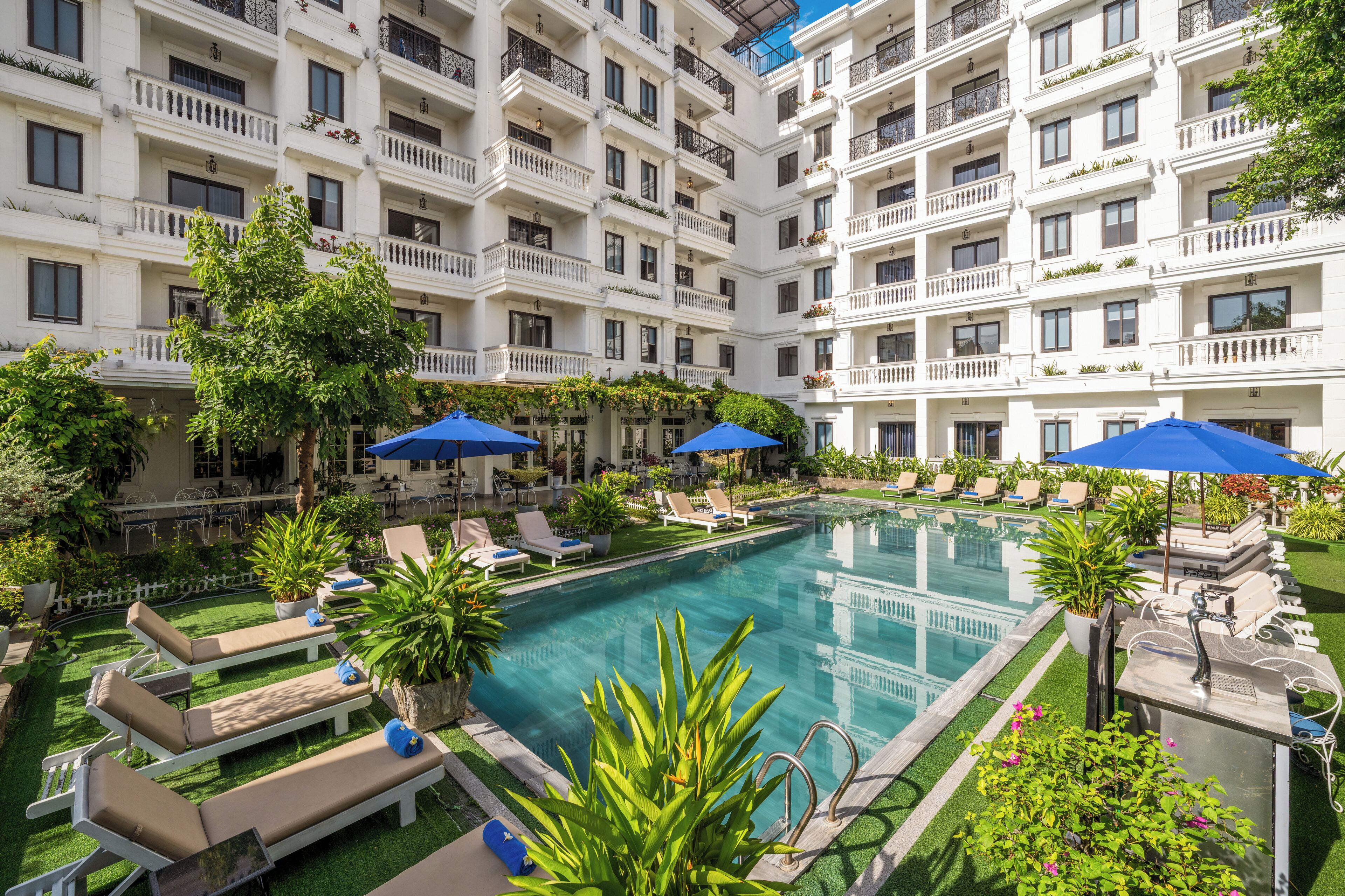 A multi-story hotel with a central swimming pool, outdoor seating, and balconies.