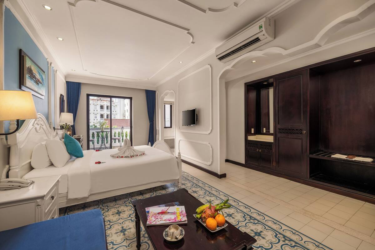 A hotel room with a bed, bedside table, lamp, and a view of the city.