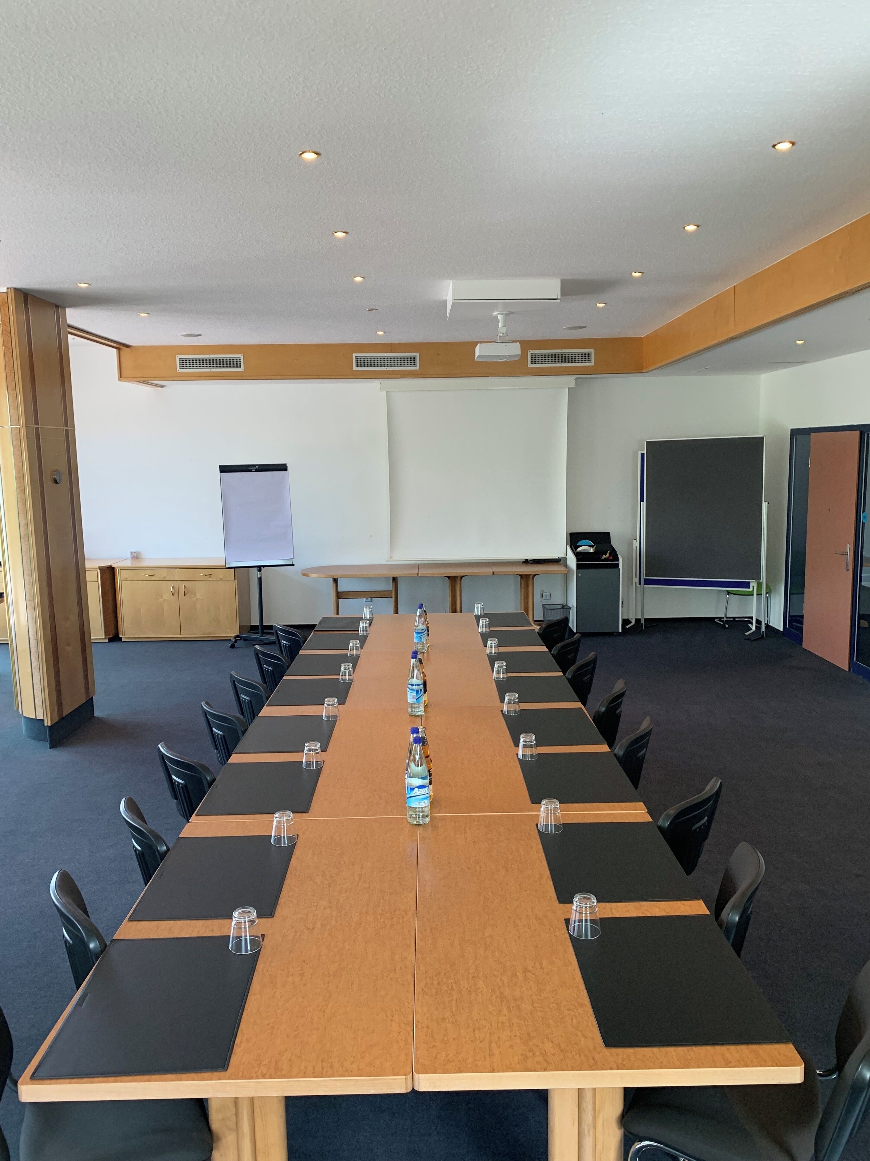 A conference room with a long table, chairs, a projector screen, and a whiteboard.